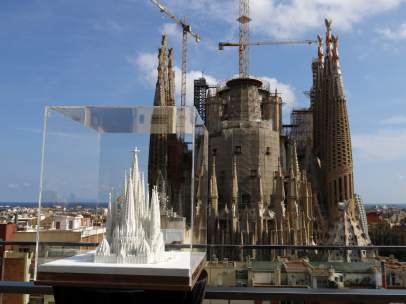 Una maqueta de la Sagrada Familia con las torres acabadas y, al fondo, el templo a día de hoy.