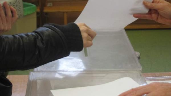 Una mano deposita una papeleta en la urna en un colegio electoral Una mano deposita una papeleta en la urna en un colegio electoral