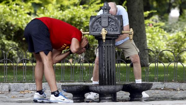 Dos personas se refrescan en una fuente por el calor Dos personas se refrescan en una fuente por el calor