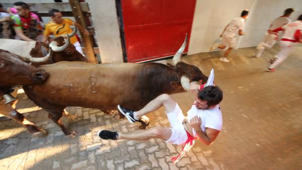 Encierro de Sanfermines. Corredor colgando por el pañuelo de un miura. Encierro de Sanfermines. Corredor colgando por el pañuelo de un miura.
