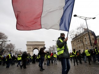Un hombre con chaleco amarillo porta bandera francesa en una manifestación