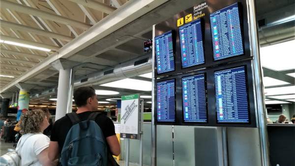Dos viajeros consultan la información de vuelos en las pantallas del aeropuerto Dos viajeros consultan la información de vuelos en las pantallas del aeropuerto