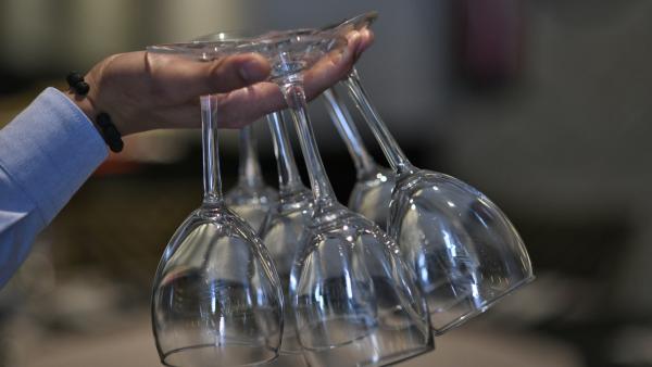 Un camarero sujeta copas de vino de cristal entre sus dedos Un camarero sujeta copas de vino de cristal entre sus dedos