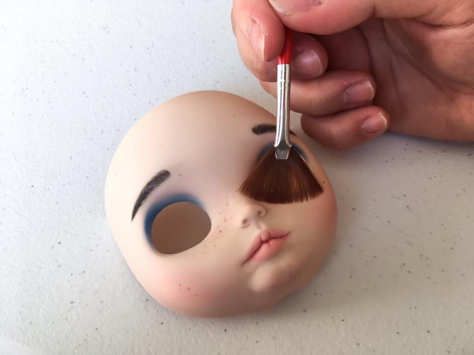 Una customizadora maquillando la cara de una Blythe.