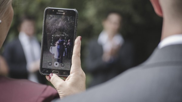 Una invitada a una boda fotografiando a los novios con su móvil Una invitada a una boda fotografiando a los novios con su móvil