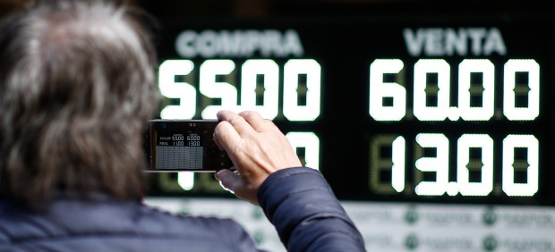 Un hombre toma una fotografía de los valores de compra y venta de la moneda argentina en Buenos Aires